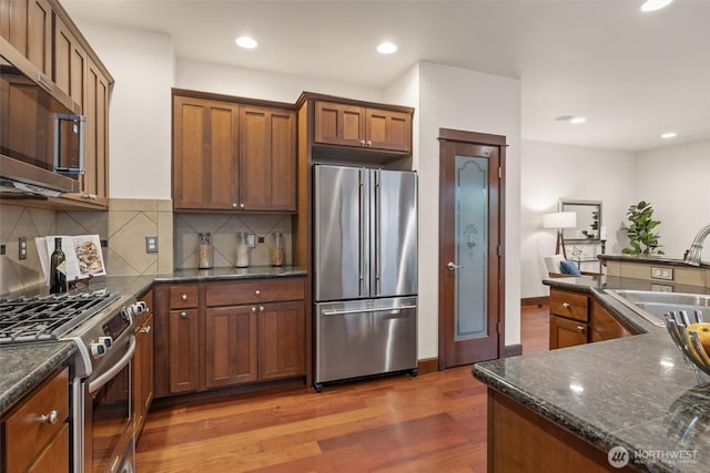 kitchen featuring stainless steel appliances, a sink, wood finished floors, tasteful backsplash, and recessed lighting