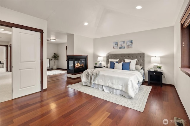 bedroom with wood finished floors, baseboards, vaulted ceiling, recessed lighting, and a multi sided fireplace