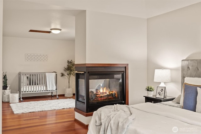 bedroom featuring wood finished floors and a multi sided fireplace