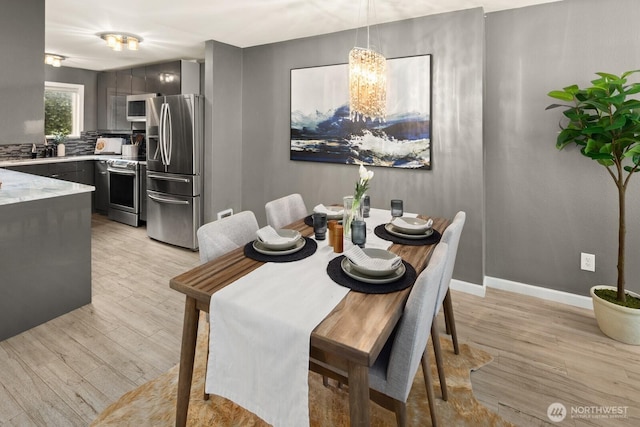 dining area featuring light wood-style flooring, a chandelier, and baseboards