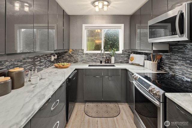 kitchen with appliances with stainless steel finishes, a sink, gray cabinetry, tasteful backsplash, and light wood finished floors