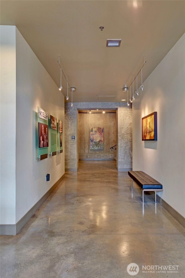 hallway with rail lighting, concrete floors, and baseboards