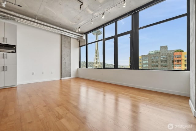 empty room with light wood-type flooring, baseboards, and a view of city
