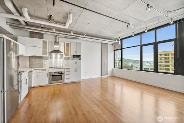 kitchen featuring stainless steel appliances, rail lighting, wall chimney range hood, light wood-type flooring, and light countertops