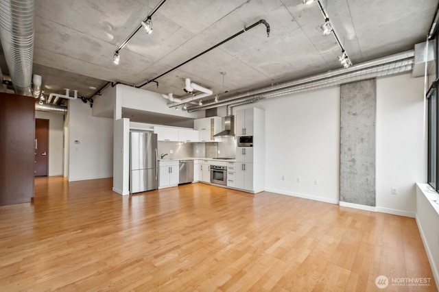 basement with freestanding refrigerator, track lighting, light wood-type flooring, a sink, and baseboards