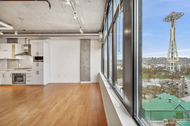 unfurnished living room with track lighting, light wood finished floors, and baseboards