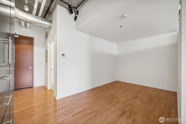 empty room featuring light wood-style flooring, baseboards, and a towering ceiling