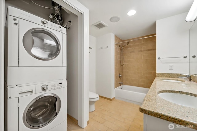 bathroom featuring stacked washer / drying machine, toilet, tile patterned flooring,  shower combination, and double vanity