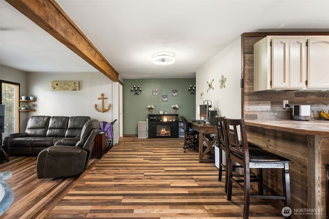 living area with wood finished floors, a warm lit fireplace, and beam ceiling