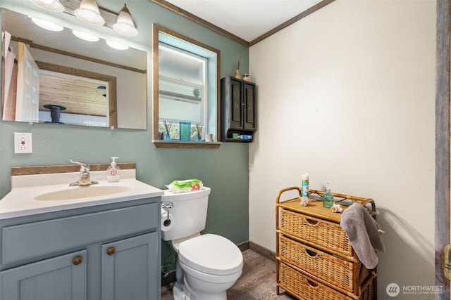 bathroom featuring toilet, wood finished floors, vanity, baseboards, and crown molding