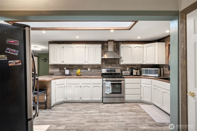 kitchen with appliances with stainless steel finishes, wall chimney range hood, white cabinets, tasteful backsplash, and recessed lighting