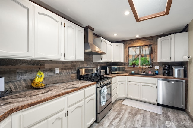 kitchen with stainless steel appliances, a sink, wall chimney exhaust hood, decorative backsplash, and white cabinets