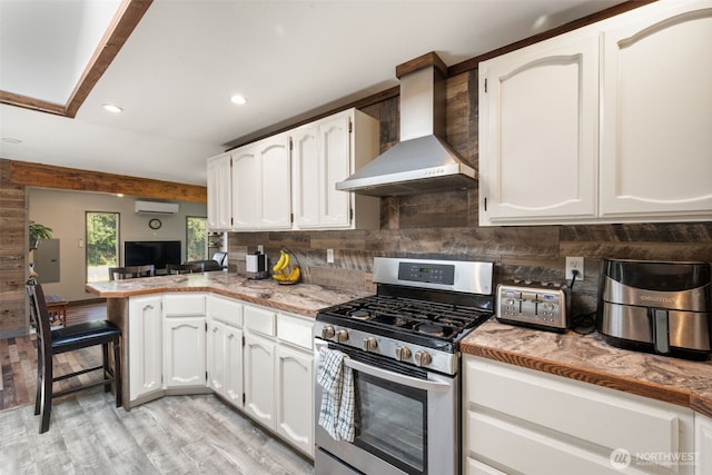 kitchen with gas stove, wall chimney exhaust hood, a peninsula, white cabinets, and light wood finished floors