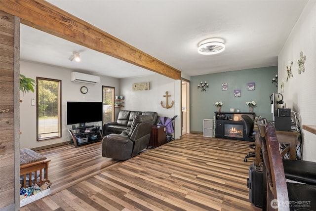 living area featuring wood finished floors, an AC wall unit, beamed ceiling, and baseboards