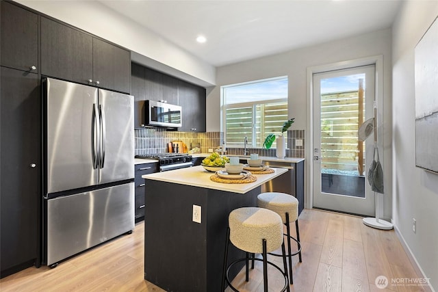 9752A Holman Rd NW, Seattle, WA 98117 - kitchen featuring stainless steel appliances, a kitchen breakfast bar, light wood-style floors, light countertops, and recessed lighting