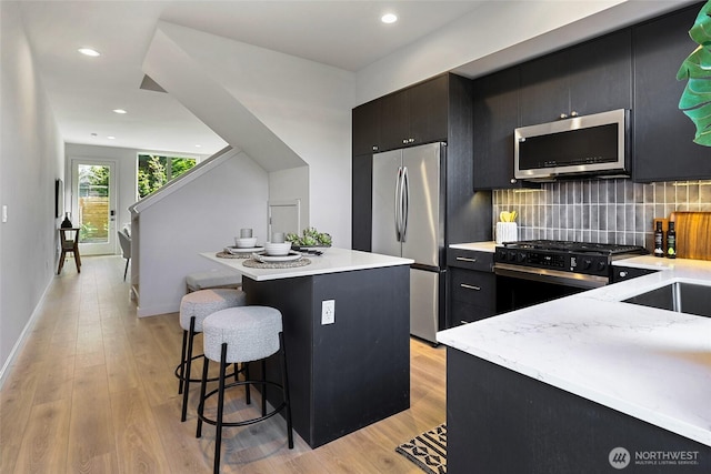 9752A Holman Rd NW, Seattle, WA 98117 - kitchen featuring appliances with stainless steel finishes, dark cabinetry, a breakfast bar, light wood-type flooring, and a center island