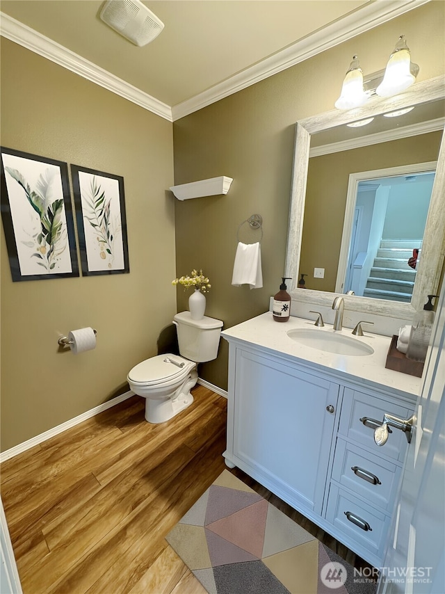 half bathroom featuring crown molding, wood finished floors, toilet, vanity, and baseboards