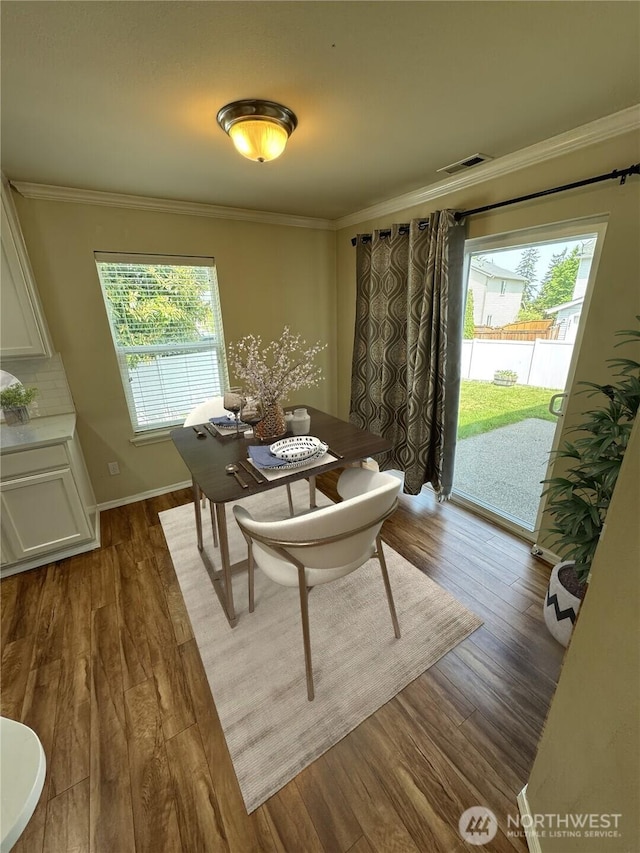 dining area with healthy amount of natural light, ornamental molding, dark wood-style flooring, and baseboards
