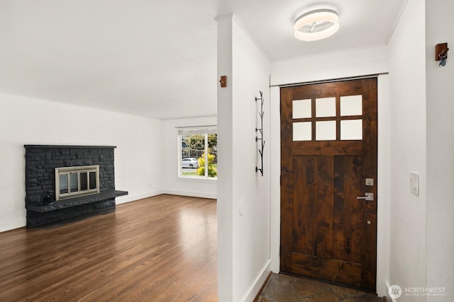 entryway featuring wood finished floors, baseboards, a stone fireplace, and ornamental molding