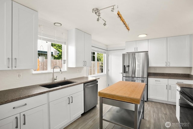 kitchen featuring a sink, appliances with stainless steel finishes, light wood-type flooring, white cabinetry, and decorative backsplash