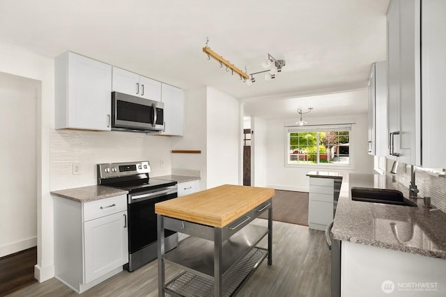 kitchen with stainless steel appliances, a sink, decorative backsplash, white cabinets, and light wood-style floors