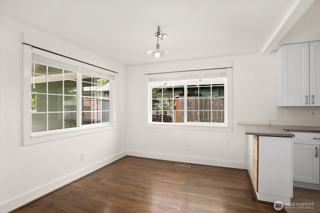 unfurnished dining area with baseboards and dark wood finished floors