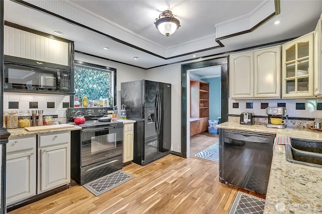 kitchen with black appliances, light wood-style floors, ornamental molding, glass insert cabinets, and a tray ceiling
