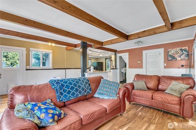 living area with light wood-type flooring, beamed ceiling, and a wainscoted wall
