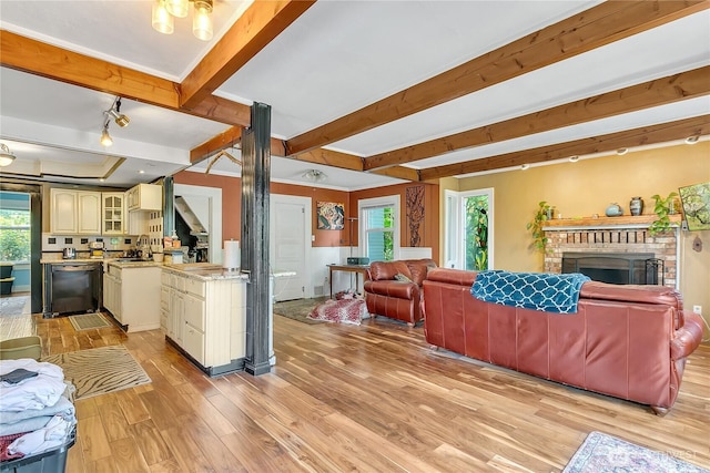 living room featuring light wood-style floors, beamed ceiling, a brick fireplace, rail lighting, and stairway