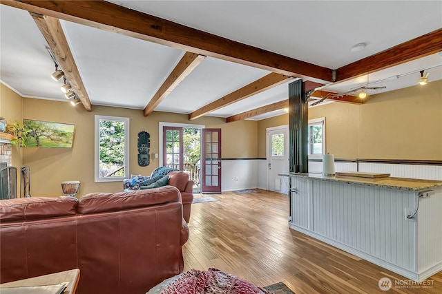 living area featuring beam ceiling, healthy amount of natural light, light wood-style flooring, track lighting, and baseboards