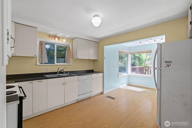kitchen with white appliances, a sink, dark countertops, and light wood-style flooring