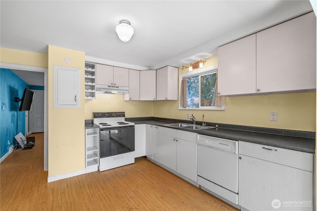 kitchen with white appliances, a sink, under cabinet range hood, light wood finished floors, and dark countertops