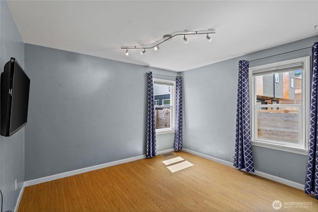 empty room with wood finished floors, baseboards, and track lighting