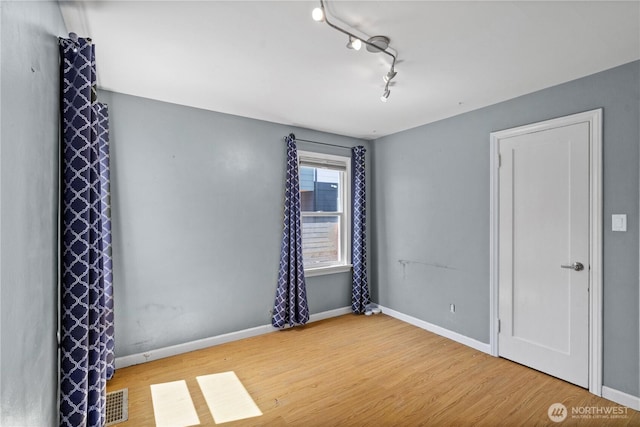 spare room with wood finished floors, baseboards, and rail lighting
