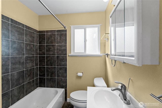 bathroom featuring a sink, toilet,  shower combination, and baseboards