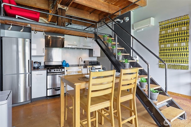 kitchen with stainless steel appliances, a wall mounted air conditioner, wall chimney range hood, white cabinets, and finished concrete flooring