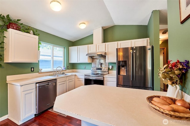 kitchen with appliances with stainless steel finishes, under cabinet range hood, a sink, vaulted ceiling, and dark wood-style floors