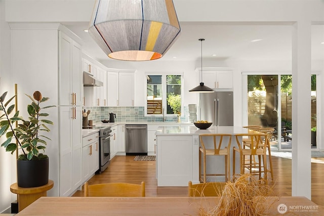 10419 41st Ave SW Unit A, Seattle, WA 98146 - kitchen featuring premium appliances, white cabinetry, a kitchen island, tasteful backsplash, and light wood-type flooring