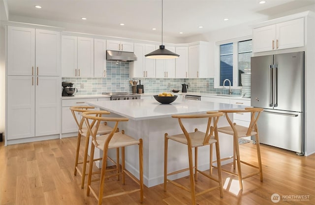 10419 41st Ave SW Unit A, Seattle, WA 98146 - kitchen with high quality fridge, under cabinet range hood, white cabinetry, a kitchen island, and a sink