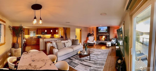 living room with wood finished floors, a stone fireplace, and a chandelier