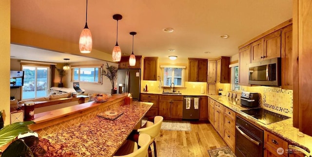 kitchen with appliances with stainless steel finishes, a sink, brown cabinets, light wood-type flooring, and recessed lighting