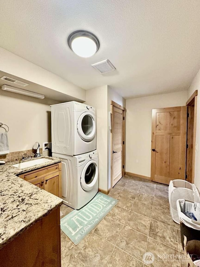 clothes washing area featuring estacked washer and dryer, cabinet space, a textured ceiling, and baseboards