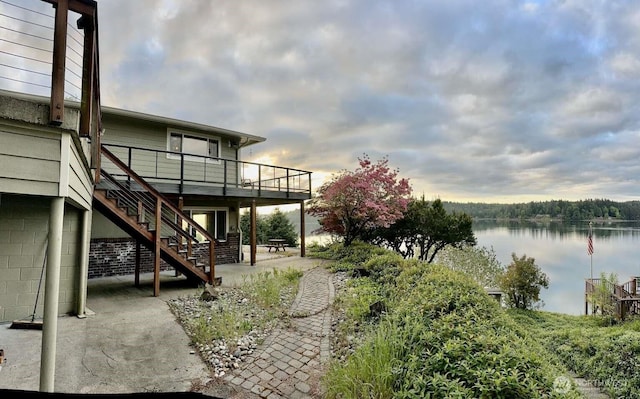 view of yard featuring a patio, stairway, and a deck with water view