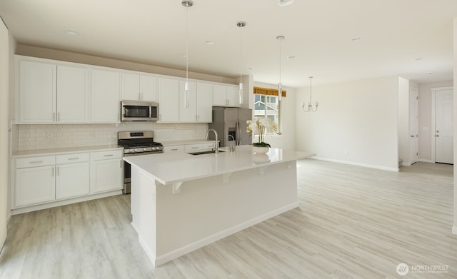 6146 Windlass Ave SE, Port Orchard, WA 98367 - kitchen with stainless steel appliances, a sink, light wood-style flooring, backsplash, and a center island with sink