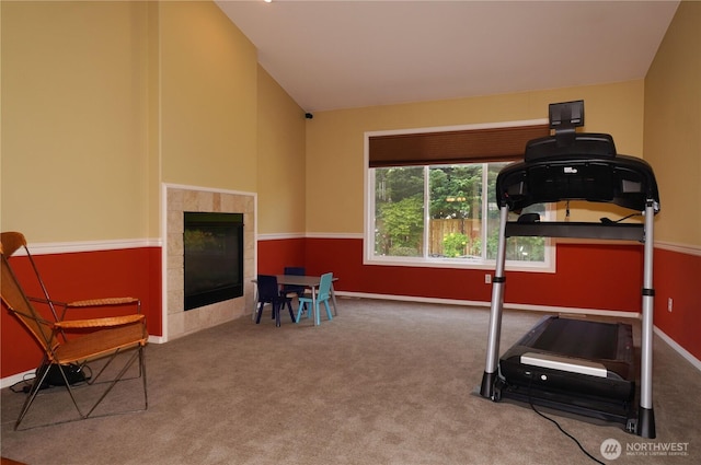 exercise area featuring carpet flooring, a tiled fireplace, lofted ceiling, and baseboards
