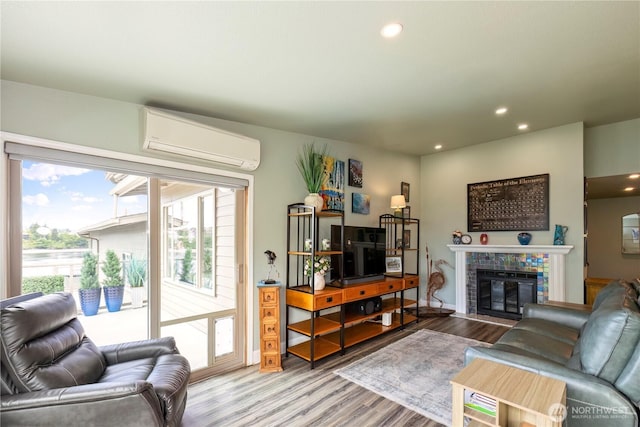 living area with an AC wall unit, wood finished floors, recessed lighting, and a tile fireplace