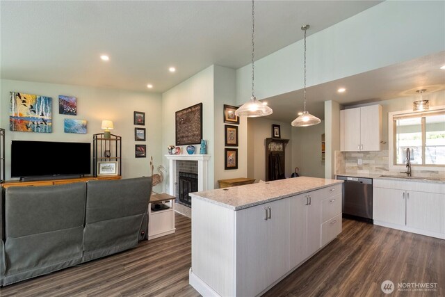 kitchen with dishwasher, a sink, open floor plan, dark wood finished floors, and a fireplace