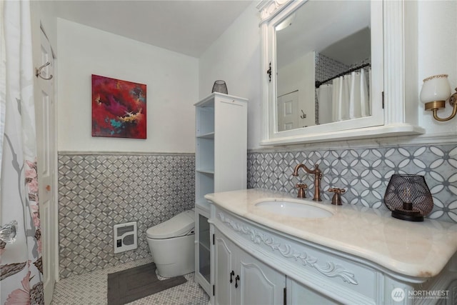 full bathroom with a wainscoted wall, toilet, vanity, tile walls, and tile patterned flooring