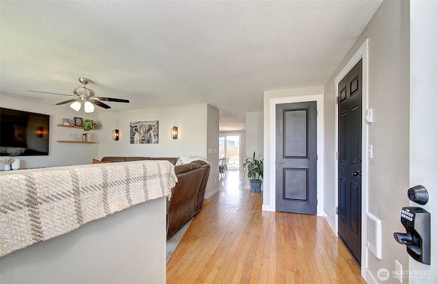 living room with light wood-style flooring, baseboards, a ceiling fan, and a textured ceiling