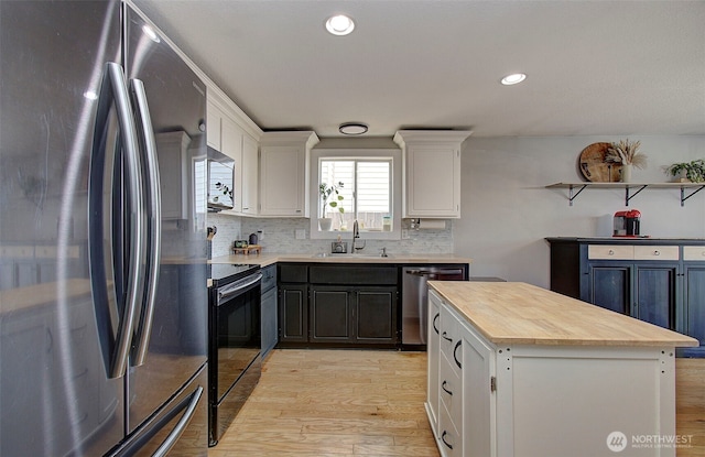 kitchen with stainless steel appliances, a sink, light wood finished floors, white cabinetry, and decorative backsplash